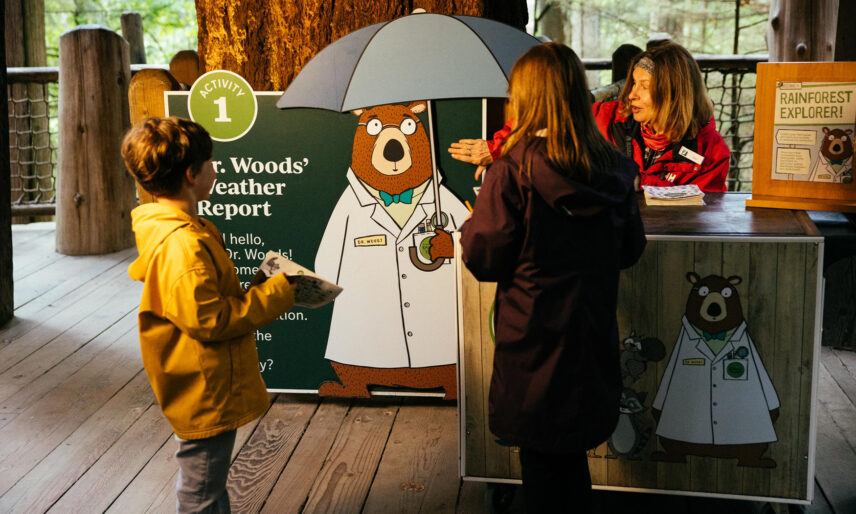 A team member from Capilano Suspension Bridge Park explains the Kids Rainforest Explorers program to two children, igniting their curiosity and enthusiasm for nature exploration and adventure