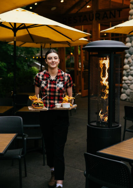 A team member walks out of the Cliff House Restaurant with plates of food in hand, ready to serve guests with delicious meals and warm hospitality at Capilano Suspension Bridge Park