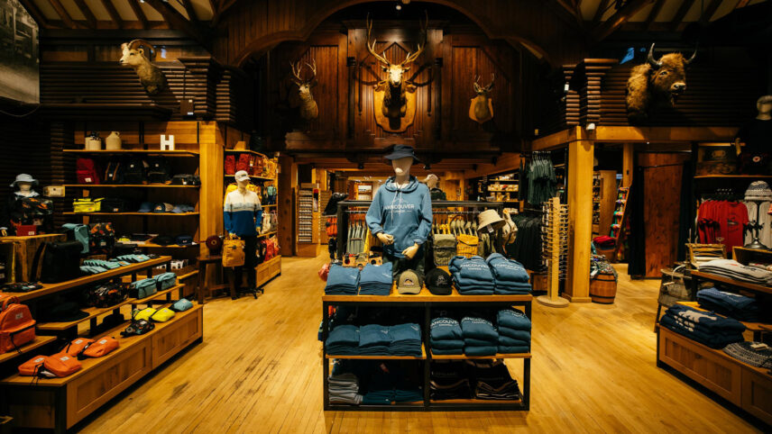 The grand entrance of the Trading Post Gift Shop features wooden fixtures, mounted animal heads, and an array of clothing items, inviting guests to explore a rustic and eclectic shopping experience at Capilano Suspension Bridge Park