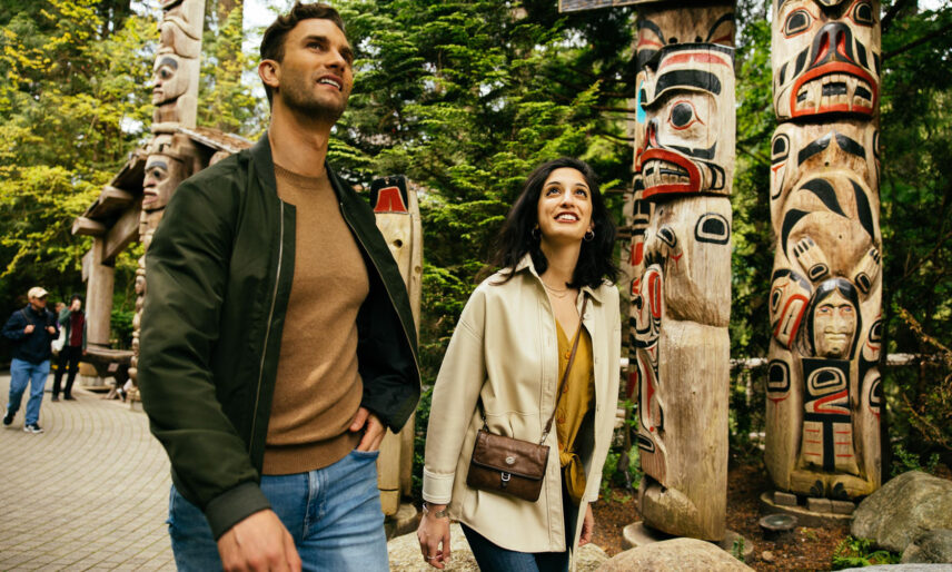A young couple explores the vibrant Kia'palano totem poles at Capilano Suspension Bridge Park, immersed in the rich cultural heritage and artistry of the Pacific Northwest