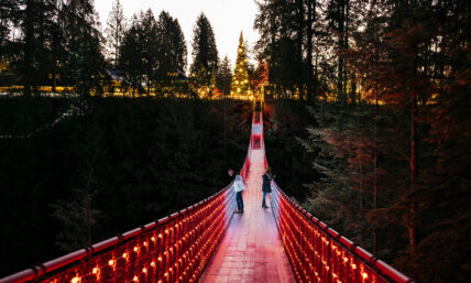 two guests looking out on the Capilano Suspension Bridge glowing red and white during Love Lights