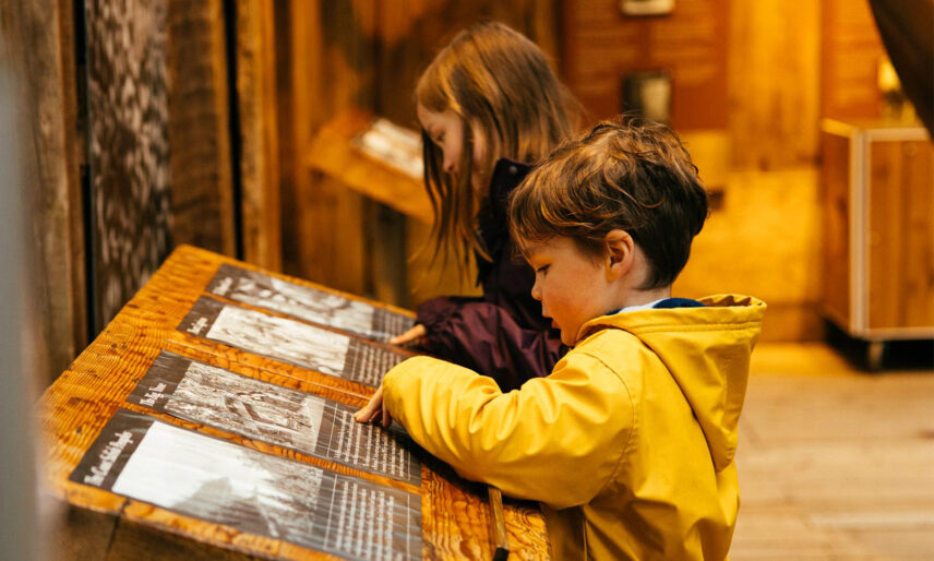 Two children engage with historical images of Indigenous peoples from North Vancouver in Kia'palano, learning about the rich cultural heritage and traditions preserved at Capilano Suspension Bridge Park